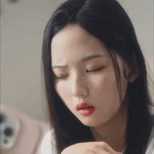 a woman with long black hair and red lips looks down