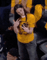 a woman in a yellow t-shirt is standing in the stands of a basketball game .