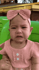 a baby wearing a headband and a pink top is crying