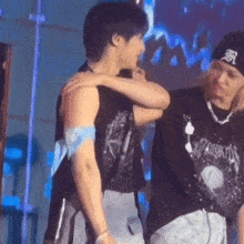 two men are hugging each other on a stage and one of them is wearing a hat .