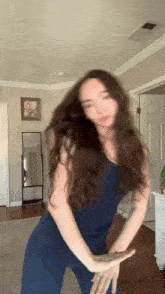 a woman in a blue top and pants is dancing in a room