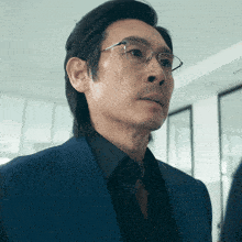 a man wearing glasses and a blue suit looks to his left