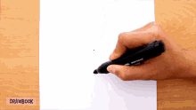 a person is drawing on a piece of paper with a drawbook in the background