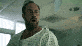 a man in a hospital gown is standing in a hospital room with his mouth open .