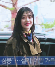 a woman wearing a trench coat smiles in front of a sign that says wp.329