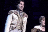 a man and a woman are on a stage and the man is wearing a white jacket