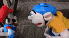 two stuffed animals , one wearing a blue helmet , are standing next to each other on a sidewalk .
