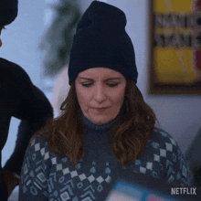 a woman wearing a beanie and a sweater is looking down at something .