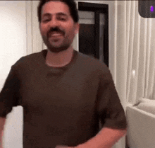 a man with a beard is standing in a living room with his arms outstretched .