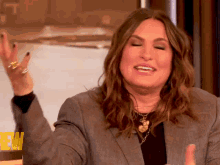 a woman wearing a gray jacket and black shirt is smiling and making a gesture with her hand