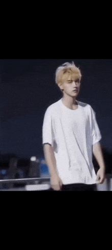 a young man with blonde hair is wearing a white t-shirt and standing in front of a black background .