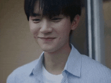 a close up of a young man wearing a blue striped shirt smiling .
