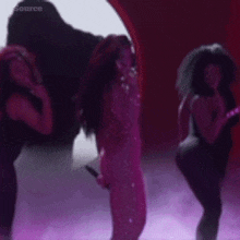 a woman is singing into a microphone while two other women are dancing in front of her .