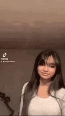 a woman with long hair and bangs is standing in a room with a guitar in the background .