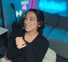 a woman is sitting in front of a neon sign that says hustle