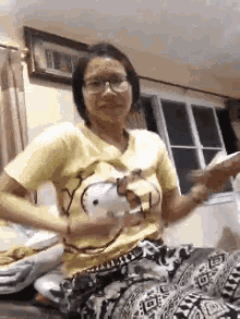 a woman is sitting on a bed wearing a hello kitty shirt and glasses .