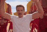 a man with a mustache is wearing a white t-shirt and raising his arms in the air