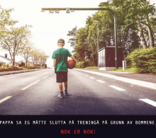 a boy is holding a basketball on the side of the road