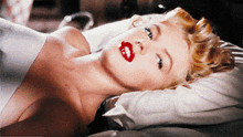 a woman with red lipstick is laying down on a bed