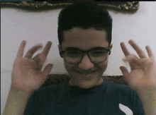 a young boy wearing glasses and a blue shirt is making a peace sign with his hands
