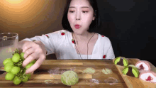 a woman is eating a bunch of green grapes on a wooden cutting board