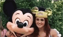 a woman is posing for a picture with mickey mouse at disneyland .