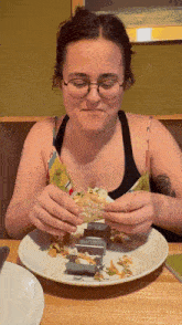 a woman wearing glasses is eating a sandwich on a white plate
