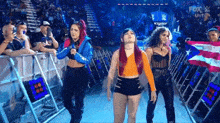 a group of women are standing in a ring in front of a crowd at a wrestling event .