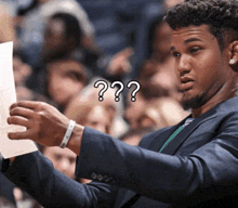 a man in a suit holds a piece of paper in front of a crowd with a question mark on his face