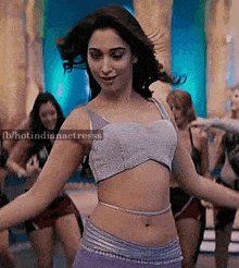 a woman in a crop top and purple pants is dancing in front of a crowd .