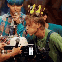 a man wearing a crown is blowing out a candle on a cake while another man holds a microphone .