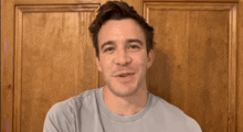 a man in a blue t-shirt is smiling in front of a wooden wall .