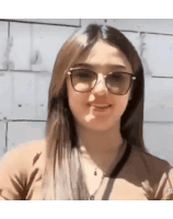 a woman wearing glasses and a necklace is smiling in front of a wall .