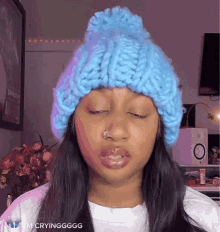 a woman wearing a blue knitted hat is making a funny face with her eyes closed .