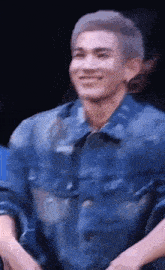 a man in a blue denim jacket is smiling while sitting down .