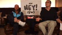 two men sit on a couch with a sign that says hey on air