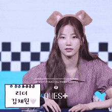 a girl wearing a bear ear headband sits at a table in front of a sign that says quest all rights reserved