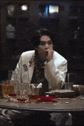 a man in a white jacket is sitting at a table with glasses of alcohol