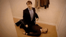 a man in a suit is kneeling next to another man laying on the floor .