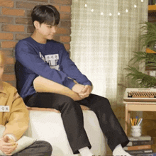 a man in a blue shirt is sitting on a couch next to another man in a yellow jacket .