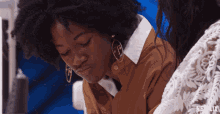 a woman wearing hoop earrings sits next to a woman wearing a white lace top with netflix written on the bottom