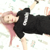 a woman with pink hair is laying on a bed wearing a black ouais shirt