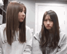 two girls are standing next to each other and looking at each other . one of the girls is making a funny face .