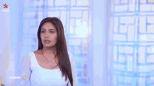 a man with a beard wearing a white shirt is standing in front of a curtain .