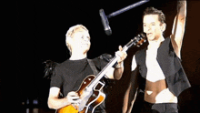 a man is playing a guitar while another man sings into a microphone on a stage .