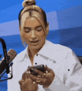 a woman in a white shirt is looking at her cell phone .