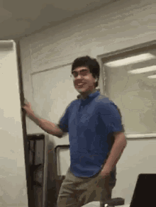 a man in a blue shirt and glasses is standing in front of a whiteboard .