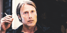 a close up of a man smoking a cigarette with a black shirt on