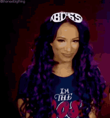 a woman with purple hair and a tiara on her head is smiling and wearing a black shirt .