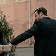 a man in a suit is holding a woman 's hand in front of a building